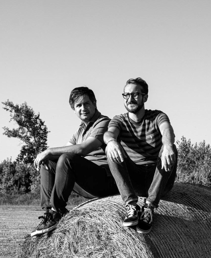 i due fondatori dello studio seduti sopra ad una balla di fieno